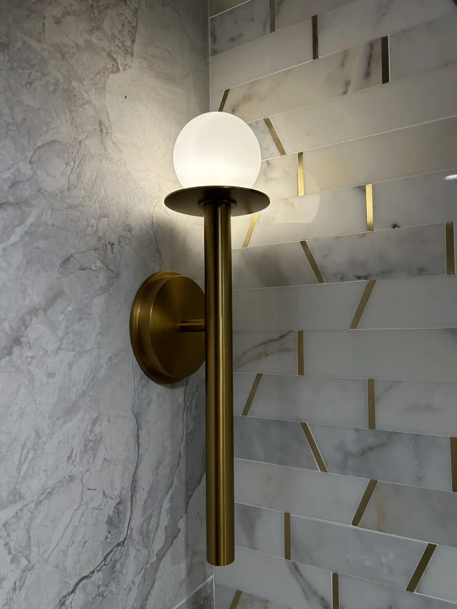 Brass globe wall sconce installed on marble tile in a Bellevue high-rise condo bathroom by HB Power Electric