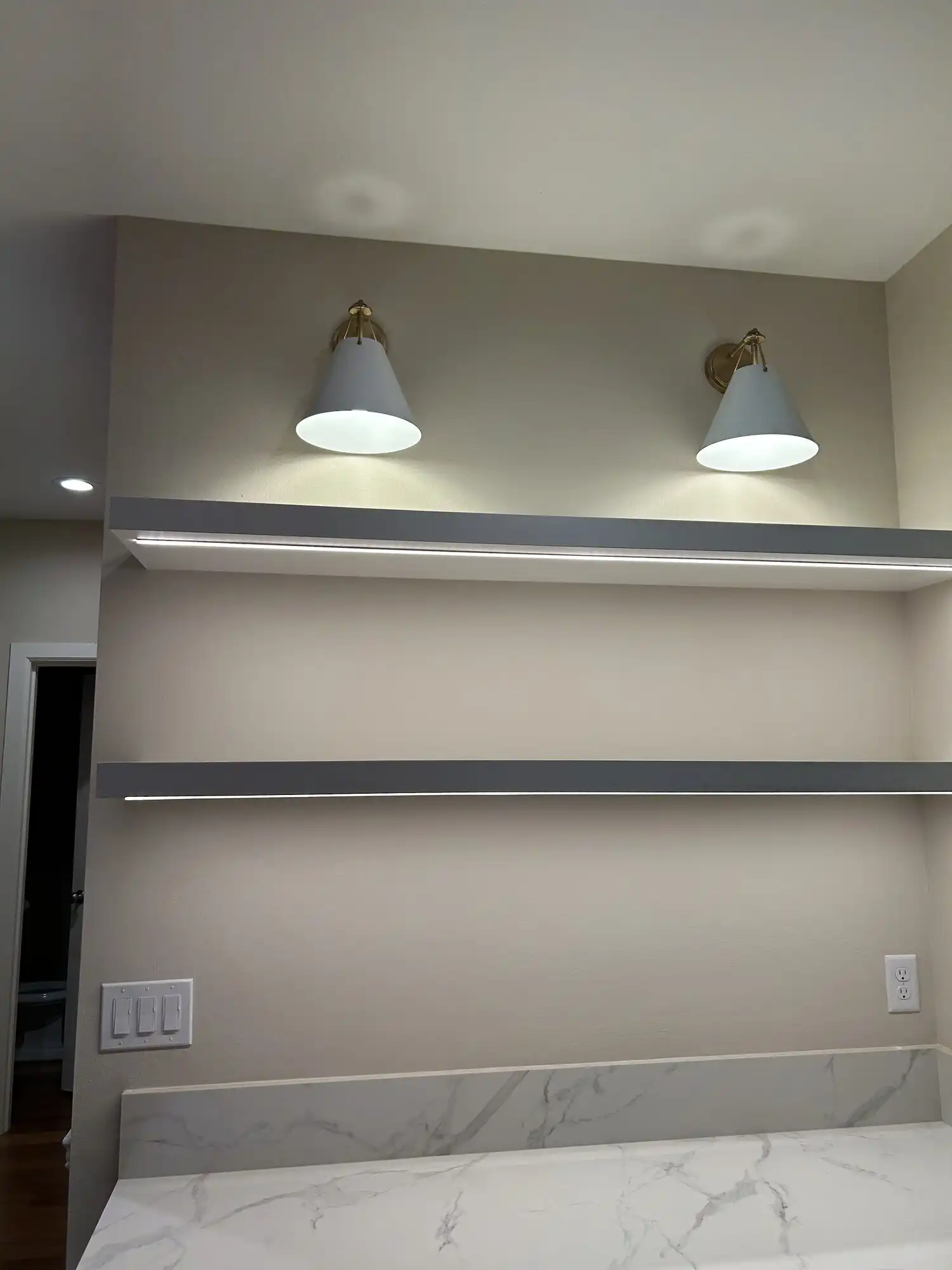 Floating shelves with under-shelf LED strip lighting and brass wall sconces installed by an electrician in Sammamish, WA